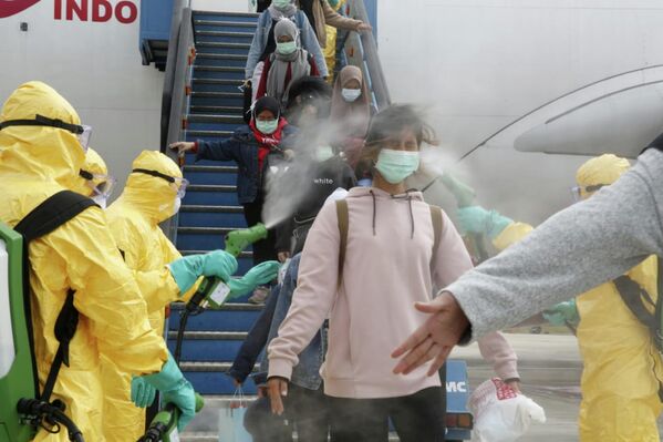 Медицинские работники опрыскивают индонезийских граждан антисептиком после того, как они прибыли из Уханя, в аэропорту Ханг-Надим