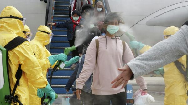 Медицинские работники опрыскивают индонезийских граждан антисептиком после того, как они прибыли из Уханя, в аэропорту Ханг-Надим