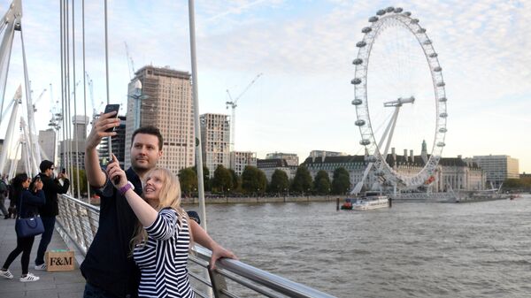 Туристы фотографируются на фоне Колеса обозрения Лондонский глаз на берегу Темзы в Лондоне