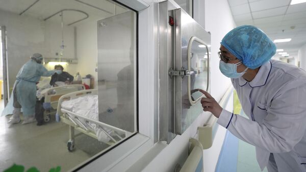 Медицинский работник смотрит за коллегой в изолированной палате больницы Цзиньинтань в Ухане