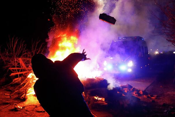 Демонстрант бросает камень в сторону полицейского фургона во время акции протеста против прибытия самолета с эвакуированными из китайской провинции Хубэй в село Новые Санжары Полтавской области