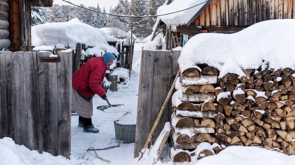 Женщина чистит снег во дворе дома в селе Омской области
