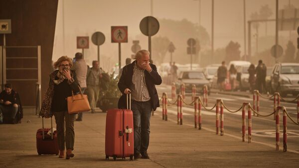 Пассажиры прикрывают в облаке красной пыли в аэропорту Санта-Крус-де-Тенерифе, Испания 