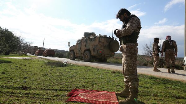 Сирийский боевик во время молитвы у дороги, по которой проезжает турецкий военный конвой в провинции Идлиб