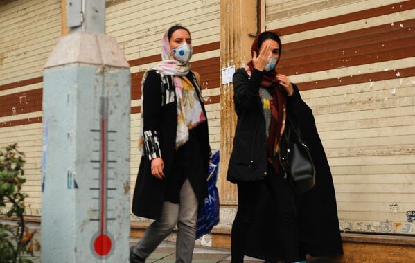 Люди в защитных масках идут по улице в центре Тегерана, Иран