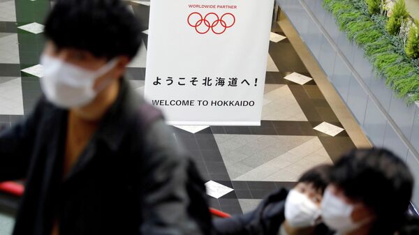 FILE PHOTO: Passengers wearing protective face masks, following an outbreak of the coronavirus, are seen near a campaign banner for Tokyo 2020 Olympic Games at New Chitose Airport in Chitose, Hokkaido, northern Japan February 27, 2020. REUTERS/Issei Kato/File Photo