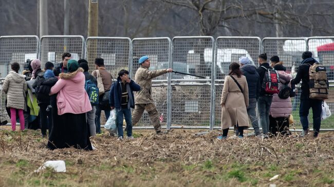 Турецкий военный и группа мигрантов в районе пограничного перехода Пазаркуле на границе Турции и Греции