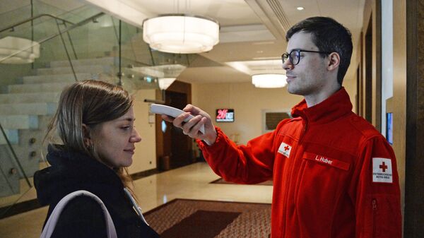 Сотрудник австрийского Красного Креста измеряет температуру журналистке в штаб-квартире ОПЕК