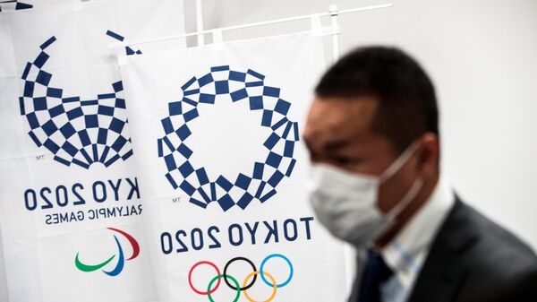 Человек в медицинской маске на фоне логотипа ОИ в Токио