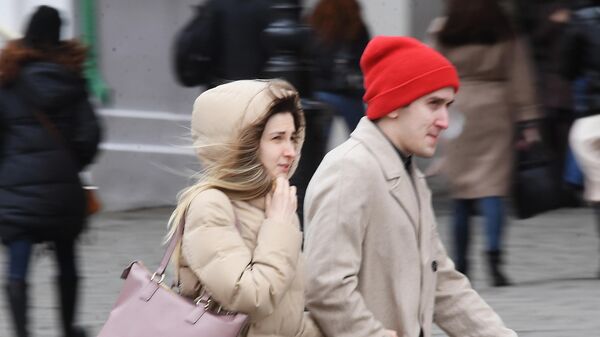 Люди идут по улице под порывами ветра в Москве