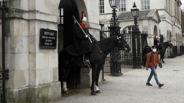 Человек в защитной маске проходит мимо Конногвардейского полка по Уайтхоллу в Лондоне, Великобритания