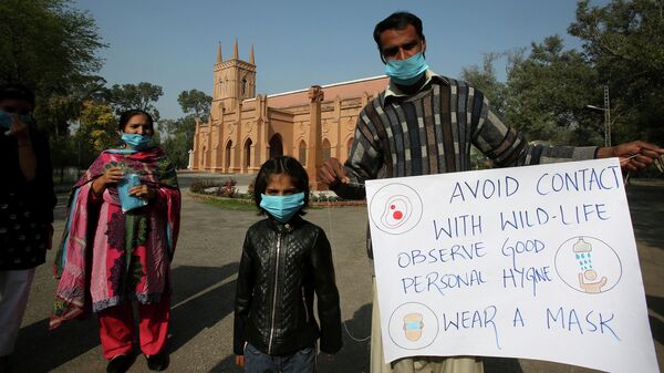 Семья держит плакат с информацией о мерах предосторожности в связи коронавирусом  перед началом мессы  в соборе Святого Иоанна в Пешаваре, Пакистан