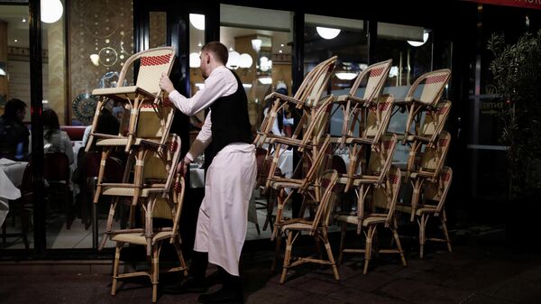 Сотрудник ресторана убирает стулья с террасы в связи с закрытием кафе и ресторанов в Париже