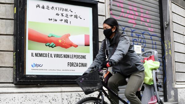 Женщина в защитной маске проезжает мимо плаката в Милане
