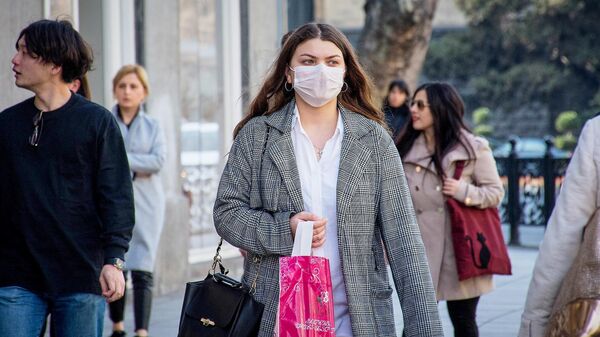Девушка идет по улице Тбилиси в медицинской маске