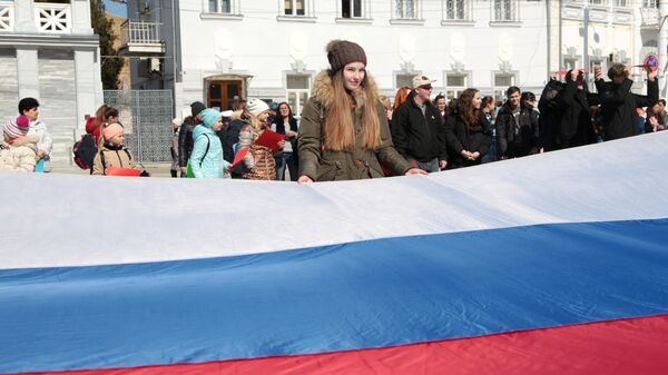 Участники флешмоба, посвященного шестой годовщине воссоединения Крыма с Россией, разворачивают флаг России в центре Евпатории