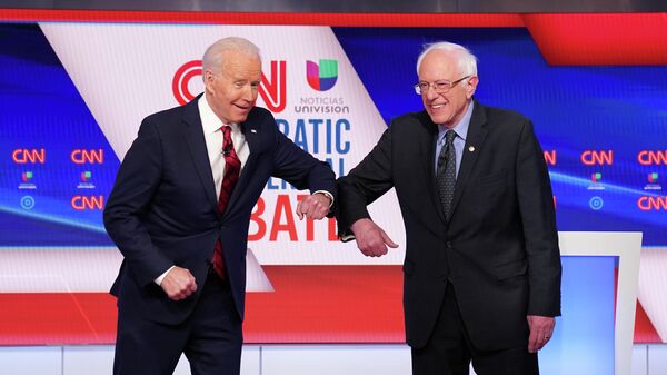 Кандидаты в президенты США Джо Байден и Берни Сандерс касаются друг друга локтями, вместо рукопожатия, перед началом предвыборных дебатов