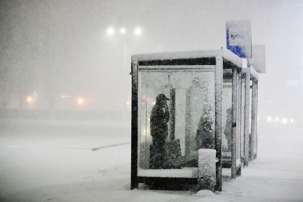 Люди на остановке общественного транспорта во время снегопада в Подольске