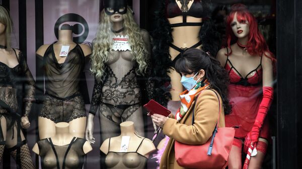 Женщина в медицинской маске проходит мимо витрины магазина в Париже