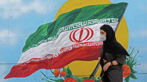 Девушка в защитной маске проходит мимо граффити с изображением национального флага в Тегеране