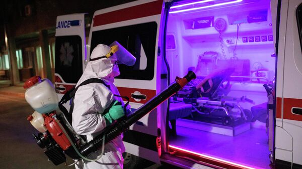 Медицинский работник в защитном костюме дезинфицирует автомобиль скорой помощи в Белграде