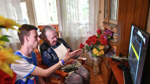 Волонтер помогает пожилой женщине в настройке телевизора