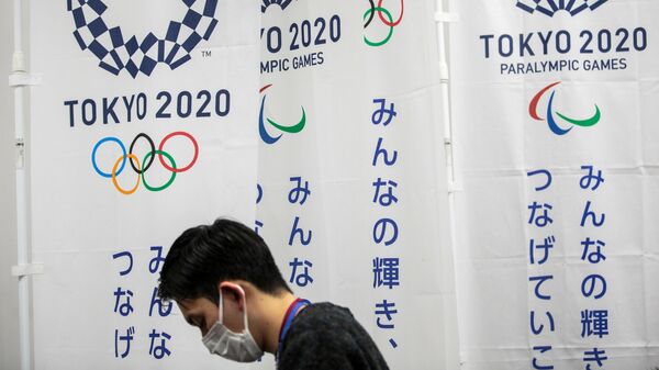 A reporter wearing a face mask stands next to the banners of the Tokyo Olympic and Paralympic Games during a Tokyo 2020 press conference about the spread of the new coronavirus in Tokyo on March 17, 2020. - Tokyo 2020 organisers said on March 17 they were scaling back certain parts of the Olympic torch relay due to the coronavirus but that spectators would be allowed to watch from the roadside. (Photo by Behrouz MEHRI / AFP)