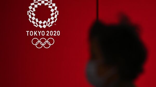 Женщина в маске проходит мимо логотипа Олимпийских игр-2020 в Токио