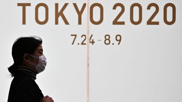 Женщина в маске проходит мимо логотипа Олимпийских игр-2020 в Токио