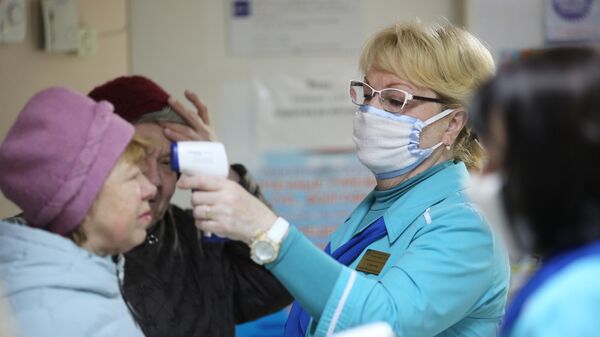 Сотрудница поликлиники  измеряет температуру посетительницы в связи с угрозой распространения коронавируса