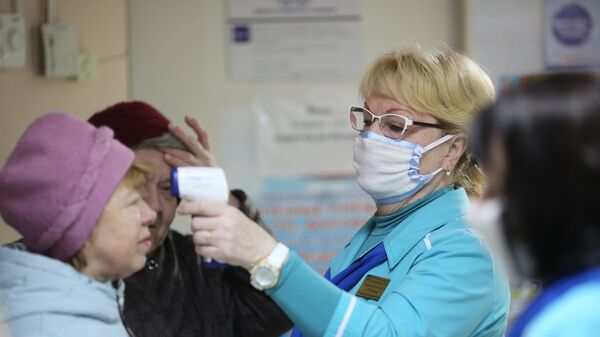Сотрудница поликлиники  измеряет температуру посетительницы в связи с угрозой распространения коронавируса