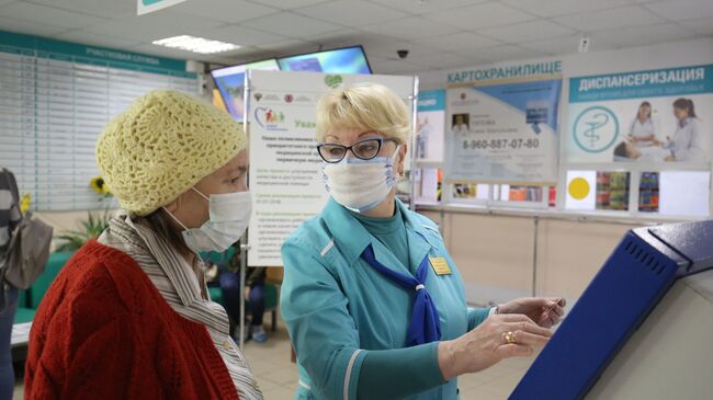 Сотрудница поликлиники  помогает посетительнице получить талон к врачу