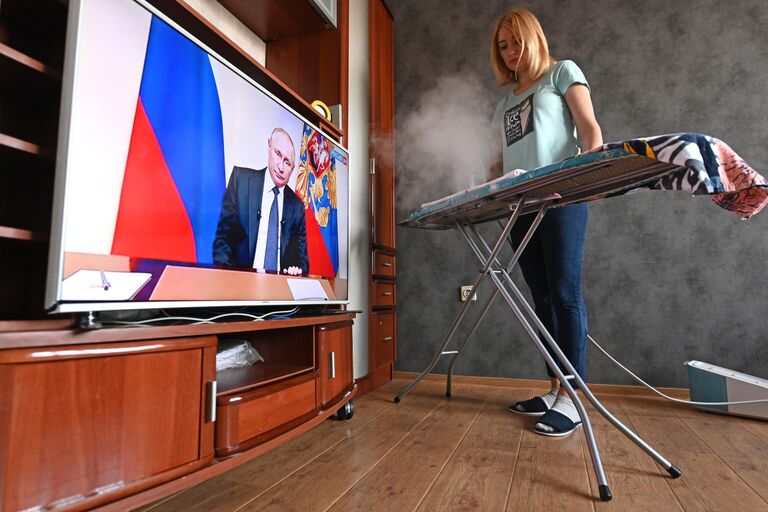Женщина гладит белье и смотрит трансляцию обращения президента России Женщина гладит белье и смотрит трансляцию обращения президента России