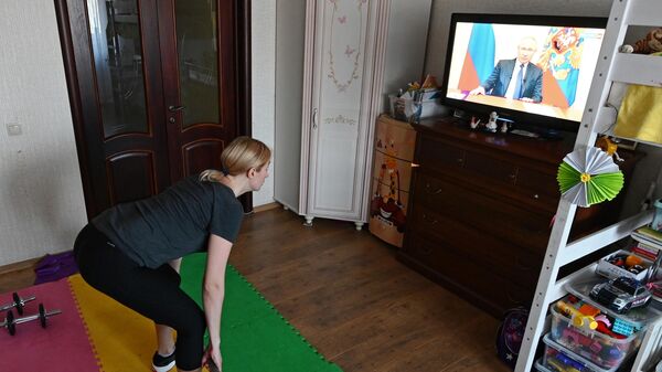 Женщина занимается спортом и смотрит трансляцию обращения президента России В. Путина к гражданам из-за ситуации с коронавирусом 