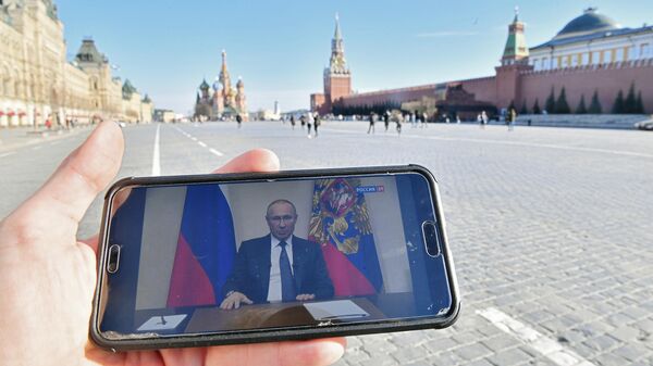 Житель Москвы смотрит на Красной площади со смартфона трансляцию обращения президента России Владимира Путина к гражданам из-за ситуации с коронавирусом