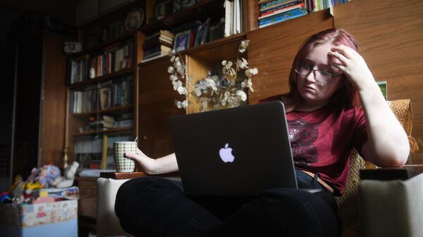 Девушка сидит на диване с ноутбуком и чаем