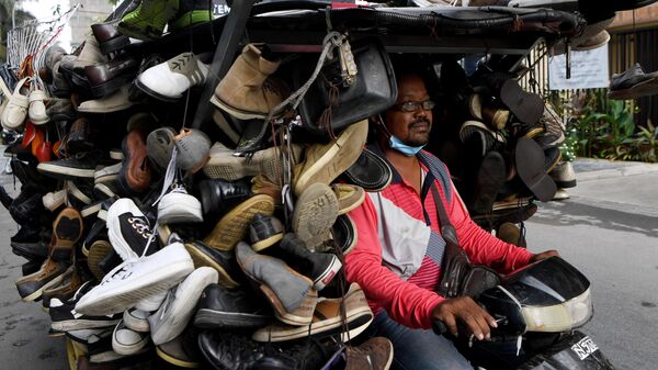 Мужчина едет на мотоцикле груженном подержанной обувью выставленной на продажу в Камбоджи