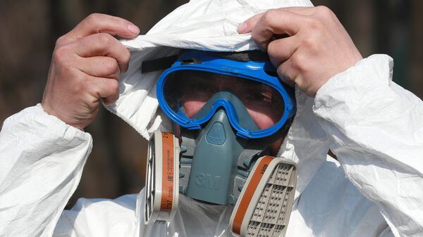 Сотрудник ГБУ Жилищник района Вешняки надевает защитный костюм перед проведением дезинфекции парковой территории от коронавирусной инфекции