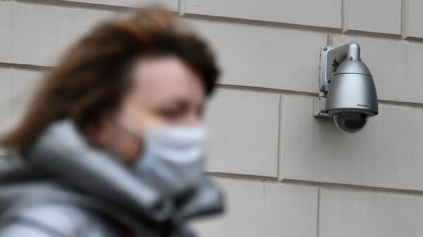 Женщина в медицинской маске проходит мимо видеокамеры на жилом доме в Москве