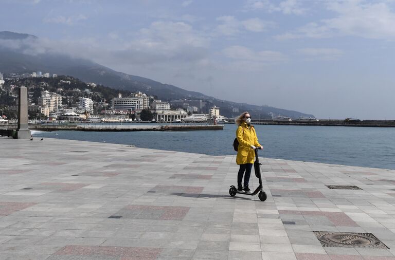 Девушка едет на электросамокате по пустой набережной в Ялте