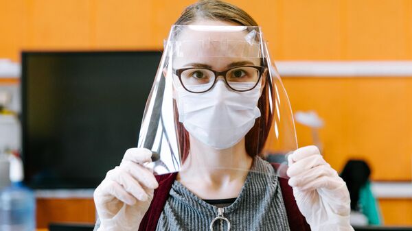 Девушка демонстрирует готовый лицевой экран для индивидуальной защиты глаз, дыхательных путей и лица медицинских работников в технопарке Кванториум. Новатория