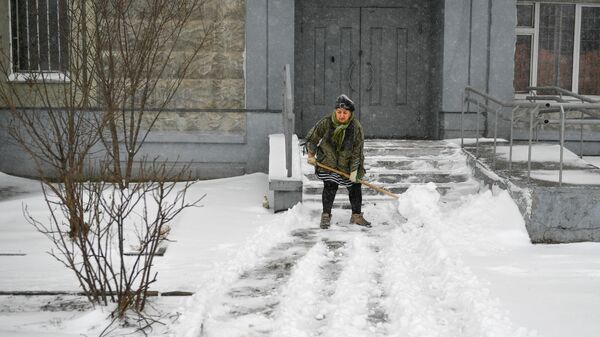 Женщина убирает лопатой снег во дворе жилого дома в Москве