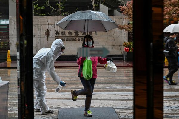 Сотрудник отеля в защитном костюме, распыляет дезинфицирующее средство на прибывшего гостя в Ухане, Китай