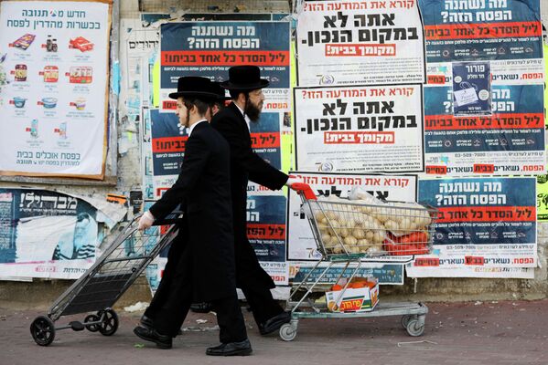 Ультраортодоксальные евреи проходят мимо информационных щитов, призывающих людей оставаться дома из-за пандемии коронавируса в Ашдоде, Израиль