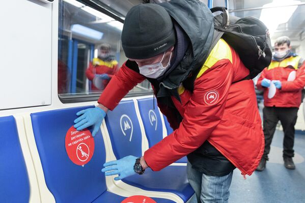 Сотрудник метро наклеивает стикер Держите дистанцию, не садитесь здесь в вагоне московского метрополитена