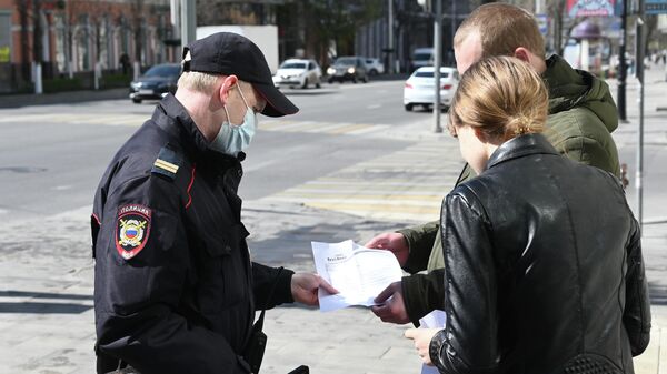 Сотрудник полиции проверяет документы у прохожих во время патрулирования улиц в целях выявления нарушителей режима самоизоляции в Ростове-на-Дону