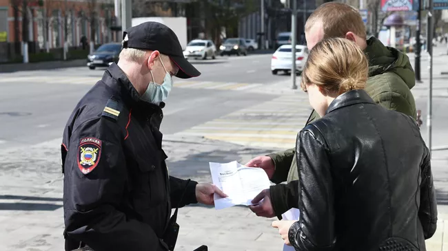 Сотрудник полиции проверяет документы у прохожих во время патрулирования улиц в целях выявления нарушителей режима самоизоляции