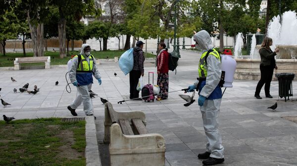 Муниципальные работники в защитных костюмах дезинфицируют площадь в Афинах, Греция