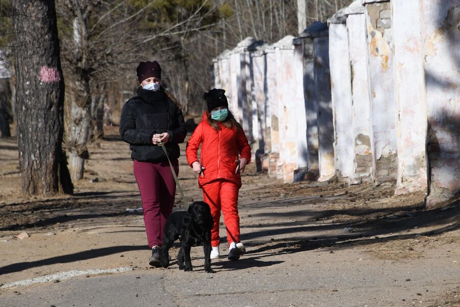 Женщина с ребенком в защитных масках выгуливают собаку на одной из улиц в Чите