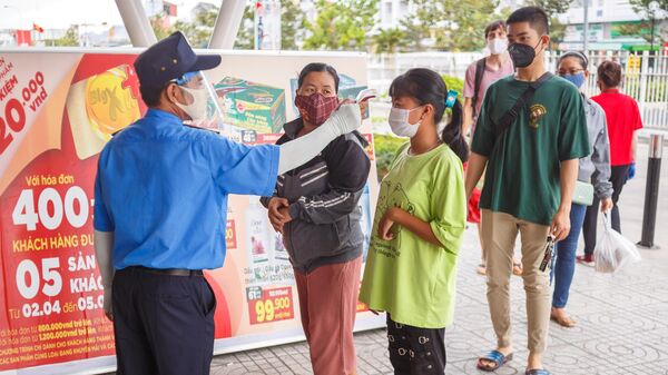Охранник измеряет температуру у покупателя на входе в супермаркет в курортном городе Нячанг во Вьетнаме